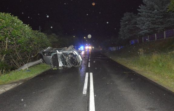 Przewrócony na drodze pojazd. W tle policyjny radiowóz