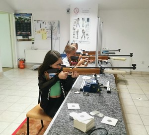 trójka dzieci mierzących do celu z broni pneumatycznej podczas zawodów strzeleckich.