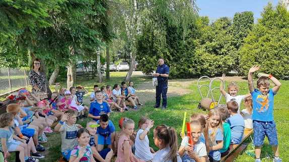 Zdjęcie kolorowe wykonane w porze dziennej - przedstawia grupę dzieci ze szkoły podstawowej w Lesznie , która bierze udział w plenerowym spotkaniu z policjantami.