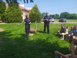 Zdjęcie kolorowe wykonane w porze dziennej - przedstawia grupę dzieci ze szkoły podstawowej w Lesznie , która bierze udział w plenerowym spotkaniu z policjantami.