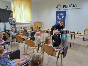 dzieci na sali narad, policjantka ubiera dziecko w umundurowanie policjanta zabezpieczającego mecze piłkarskie