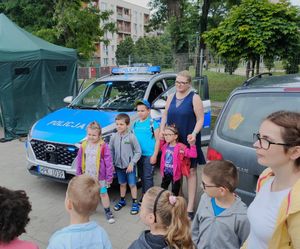 Dzieci i kobieta pozują do zdjęcia na tle radiowozu