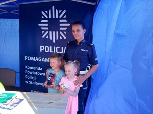 Na zdjęciu znajduje się umundurowana policjantka z dzieckiem na tle baneru z napisem Policja