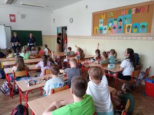 Na zdjęciu znajdują się dwie policjantki oraz dzieci siedzące w ławkach szkolnych w sali lekcyjnej