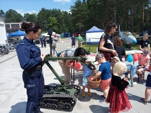 Na zdjęciu znajduje się umundurowana policjantka wraz z dziećmi oraz wojskowy robot w porze dziennej