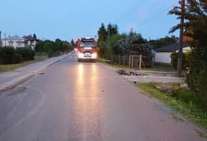 przewrócony motocykl na miejscu zdarzenia, w tle wóz strażacki