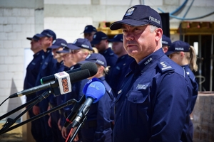 Komendant Wojewódzki Policji w Rzeszowie stoi przy mikrofonie, w tle policjanci i plac budowy.
