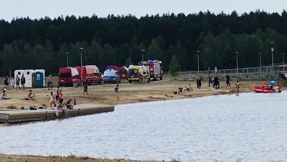 na zdjęciu zbiornik wodny. na piaszczystym brzegu wozy strażackie, radiowóz policyjny oraz wypoczywające na brzegu osoby