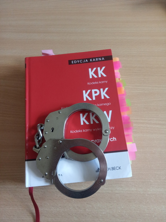 Książka kodeks karny w czerwonej okładce, na niej leżą policyjne kajdanki