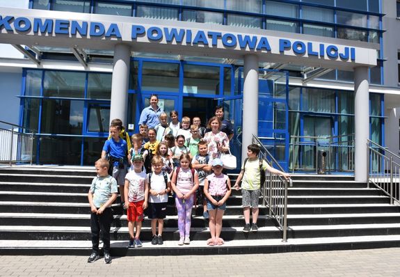 Zdjęcie grupowe dzieci, wychowawców i policjantki na tle budynku KPP Jarosław