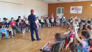 Zdjęcie kolorowe wykonane porze dziennej przedstawia grupę dzieci ze szkoły Ukraińskiej w Przemyślu która bierze udział w pogadance na temat bezpiecznych wakacji z policjantami umundurowanymi.