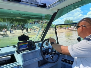 Policjant siedzący za sterami łódki w tle plaża, na której odpoczywają turyści. Plaże patroluje także patrol konny.