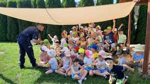 Zdjęcie kolorowe przedstawia grupę dzieci z przedszkola „Truskawkowe ranczo” w Krównikach, które biorą udział w plenerowym spotkaniu z policjantami na temat bezpiecznego wypoczynku podczas wakacji.