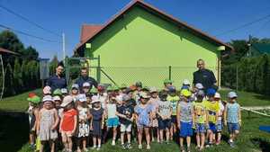 Zdjęcie kolorowe przedstawia grupę dzieci z przedszkola „Truskawkowe ranczo” w Krównikach, które biorą udział w plenerowym spotkaniu z policjantami na temat bezpiecznego wypoczynku podczas wakacji.
