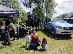radiowóz policyjny oraz policjanci na koniach przy stoisku podczas pikniku