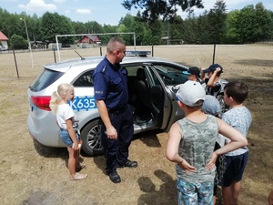 Policjant pokazuje dzieciom radiowóz, wszyscy stoją obok pojazdu