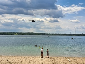 na fotografii śmigłowiec nad Jeziorem Tarnobrzeskim i przyglądający się mu ludzie