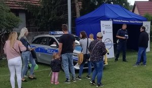 Policyjne &quot;punkt&quot; podczas festynu. Na zdjęciu widoczny namiot z logo Policji,  radiowóz oraz grupa osób