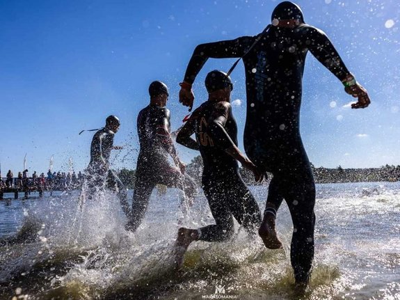 na zdjęciu czterej zawodnicy wbiegają do jeziora