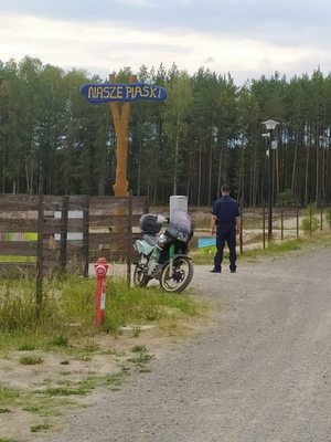 Na zdjęciu znajduje się policjant oraz motocykl przed wejściem na kąpielisko