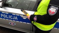 Policjant badający stan trzeźwości urządzeniem Alcoblow na tle radiowozu