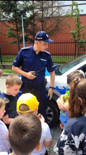 Policjant z radiostacją w ręce. Obok niego dzieci.