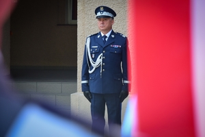 Komendant Wojewódzki Policji w Rzeszowie nadinsp. Dariusz Matusiak (widok z przodu), na pierwszym planie rozmyta biało-czerwona wstęga sztandaru.