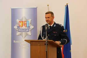 Przemawiający Pierwszy Zastępca Komendanta Wojewódzkiego Policji w Rzeszowie, w tle flagi państwowe i unijne oraz policyjne logo na niebieskim tle