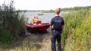 na fotografii policjant nad wodą, w tle strażacka motorówka na wodzie