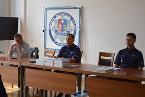 Policjanci podczas szkolenia w auli KWP w Rzeszowie. Policjanci siedzą przy stołach. Na ścianie wyświetlane są slajdy prezentacji.