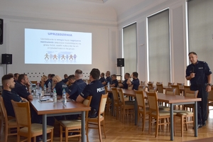 Policjanci podczas szkolenia w auli KWP w Rzeszowie. Policjanci siedzą przy stołach. Na ścianie wyświetlane są slajdy prezentacji.