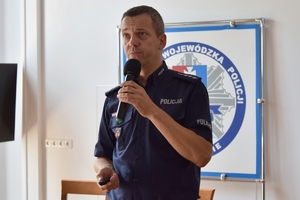 Policjanci podczas szkolenia w auli KWP w Rzeszowie. Policjanci siedzą przy stołach. Na ścianie wyświetlane są slajdy prezentacji.