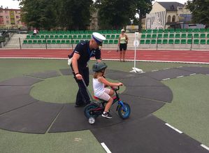 Policjant uczy dziewczynkę prawidłowej jazdy na terenie miasteczka rowerowego