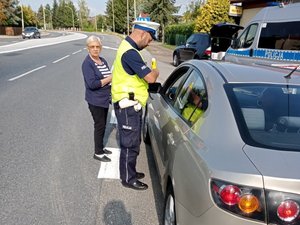 umundurowany policjant stojący przy samochodzie wykonuje sprawdzenie stanu trzeźwości kierującego,