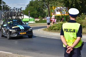 Policjant czuwa nad bezpieczeństwem kolarzy. W tle samochód przewożący na dachu rowery