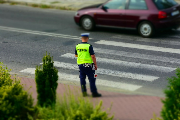 Policjant stojący przed przejściem dla pieszych i sprawdzający zachowania kierowców i pieszych.