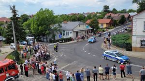 Zdjęcie wykonane z wysokości na którym widoczny jest przejeżdżający radiowóz oraz zgromadzeni ludzie