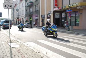 Policyjne motory bmw przejeżdżają przez ul. Jagiellońska. Nowe motocykle w kolorach żółtym, srebrnym i niebieskim. W tle ulica Jagielońska, samochody i wjeżdżający na teren komendy oznakowany radiowóz.