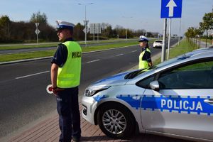 Policjanci stojący na poboczu drogi, przy radiowozie, na dalszym planie ulica, pora dzienna