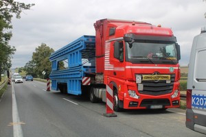 samochód ciężarowy z kabiną w kolorze czerwonym transportujący na naczepie ładunek ponagabarytowy