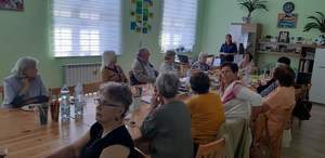 Zdjęcie kolorowe wykonane w porze dziennej przedstawia dom seniora w Dubiecku . W sali widoczni są seniorzy którzy biorą udział w spotkaniu z policjantem