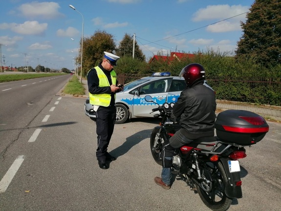 na jezdni stoi motocykl obok stoi policjant