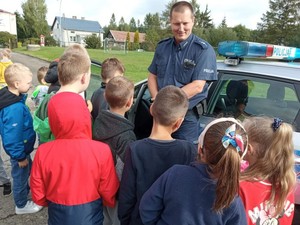 policjant przy radiowozie na szkolnym parkingu podczas spotkania z dziećmi w ramach kampanii &quot;Bezpieczna droga do szkoły&quot;