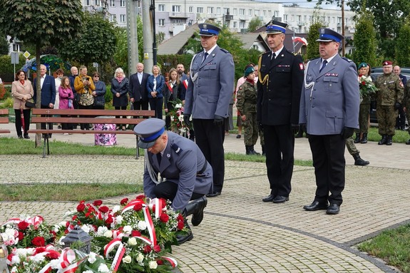 Delegacja służb mundurowych składająca wiązankę kwiatów przed pomnikiem