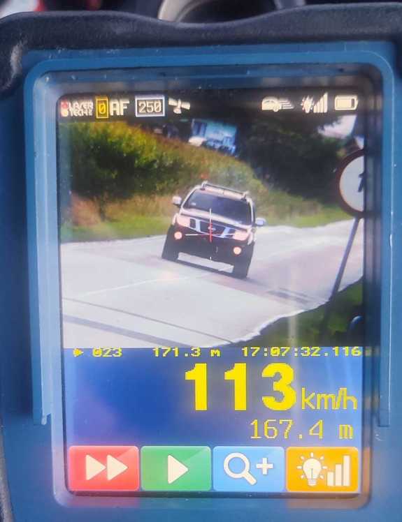 Zdjęcie kolorowe przedstawia zapis rejestratora ręcznego do pomiaru prędkości. Na wyświetlaczu widoczny jest pojazd –m-ki Nissan oraz zapis jego prędkości 113 km/h
