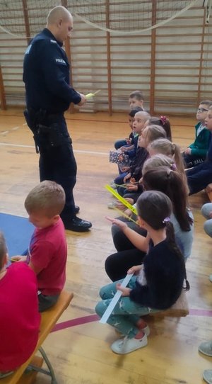Dzielnicowy Posterunku Policji w Besku na spotkaniu profilaktycznym z uczniami przekazuje elementy odblaskowe.