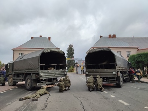Ćwiczenie PERUN 2022. na zdjęciu pojazdy wojskowe, przy nich żołnierze, w tle budynek