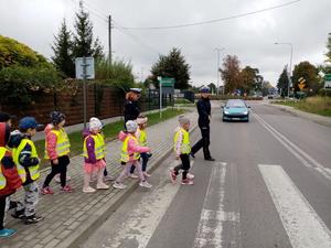 Policjantka przeprowadzająca dzieci w kamizelkach odblaskowych przez przejście dla pieszych.