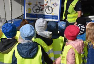 Dzieci podczas słuchają policjanta, który opowiada o bezpiecznym podróżowaniu rowerem