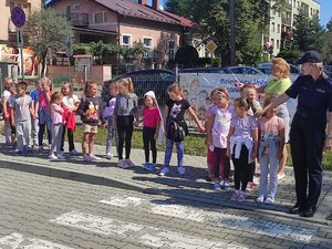na zdjęciu policjantka oraz grupa dzieci stojąca na chodniku przed przejściem dla pieszych
